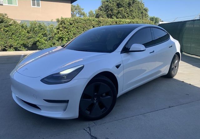 White Tesla sedan parked in a driveway with tinted windows and black wheels, viewed from the front-left side