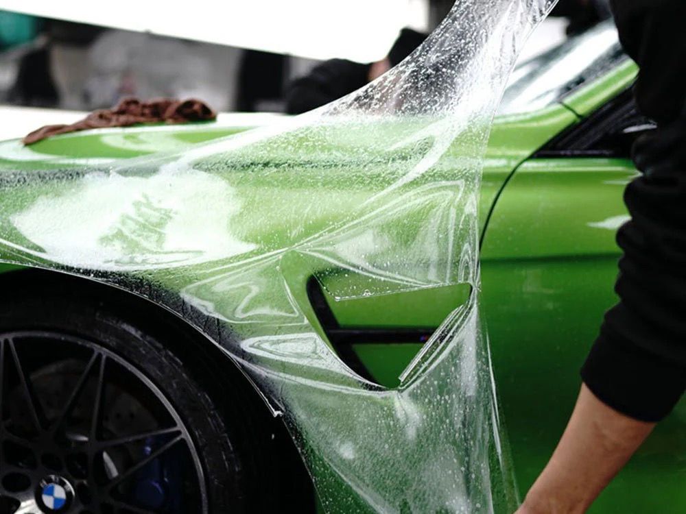 Person applying protective film to a black car's hood.