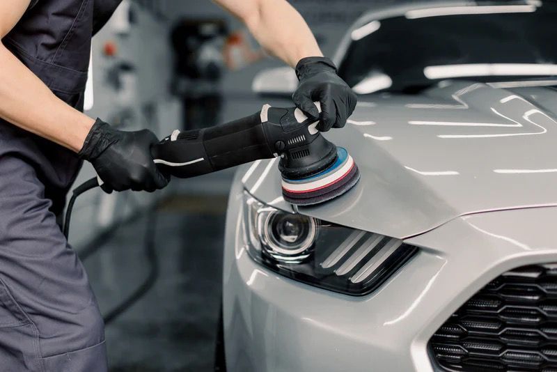 Person polishing a black car with an electric buffer.