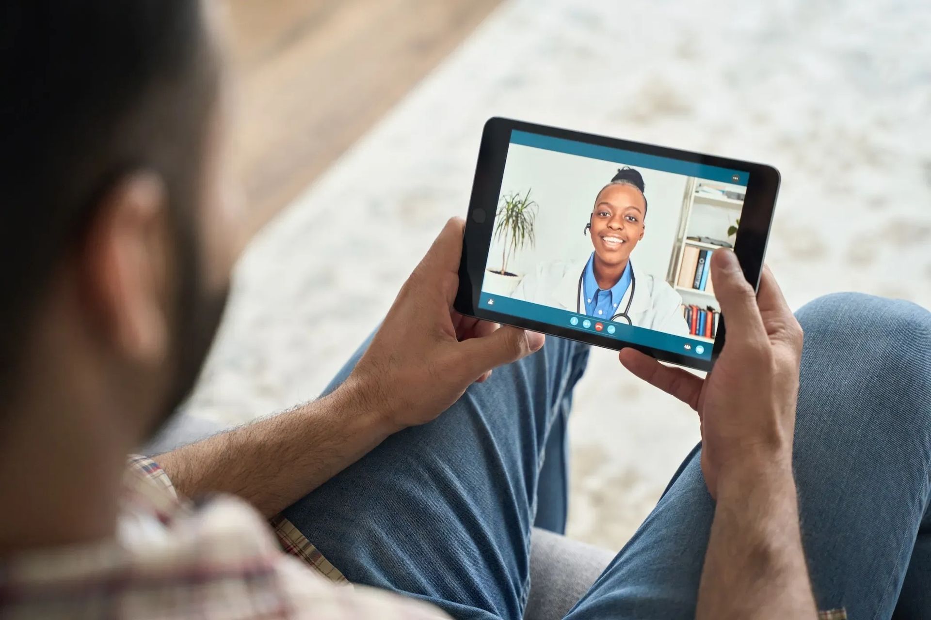 Person holding a tablet during a video call with a smiling doctor in a white coat