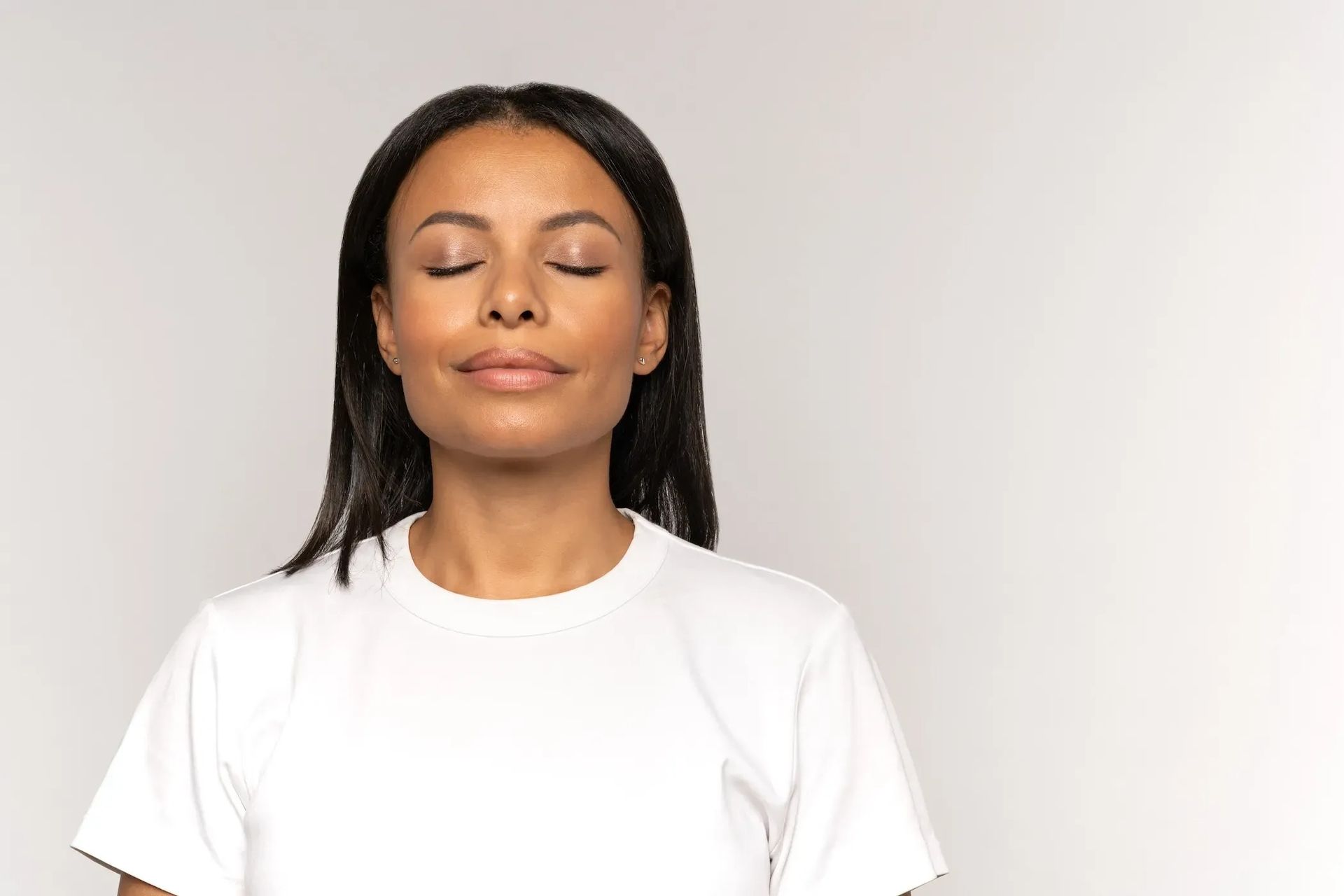 Woman with closed eyes wearing a white shirt against a light gray background