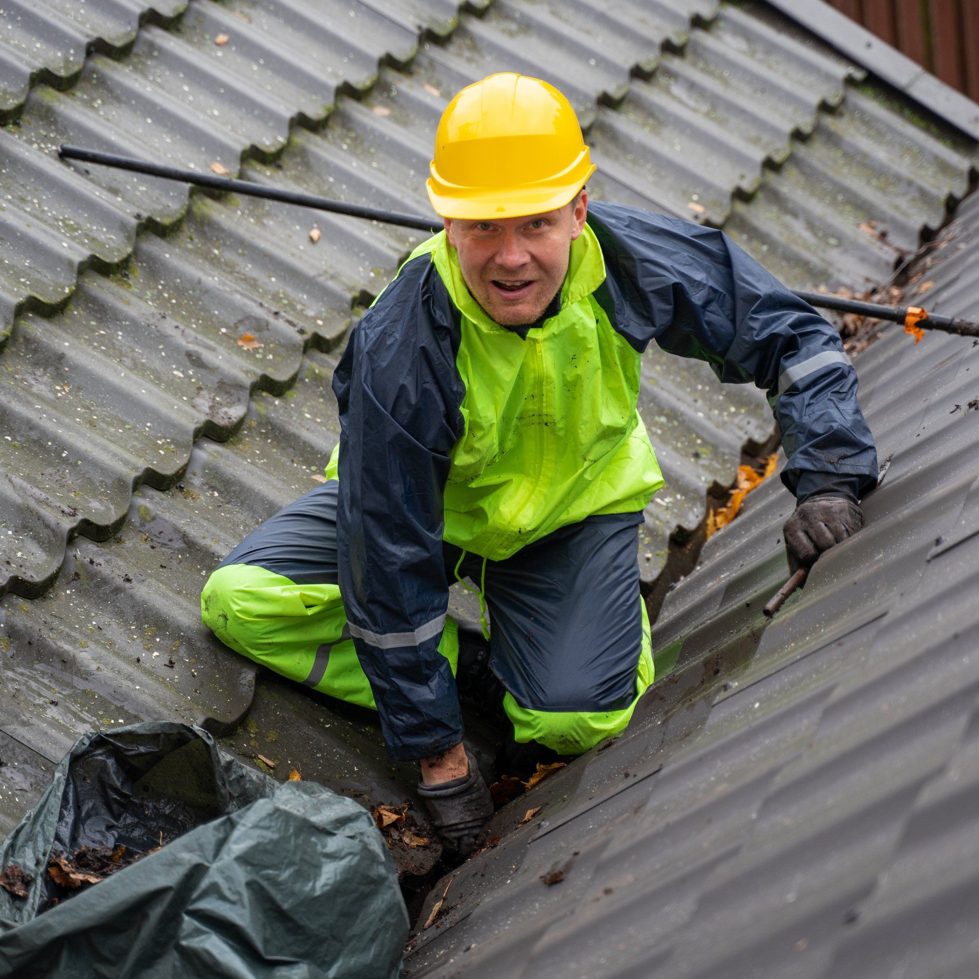 A man in a yellow hard hat is kneeling on a roof.
