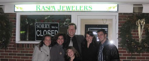 A group of six people posing and smiling in front of a storefront sign that reads