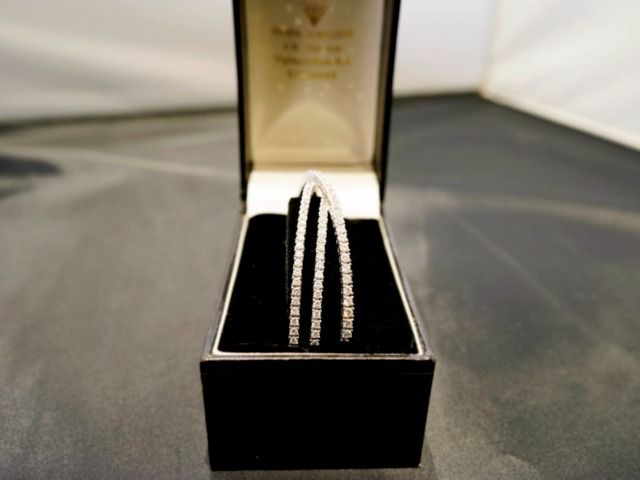 A three-row diamond tennis bracelet displayed upright in an open black jewelry box.