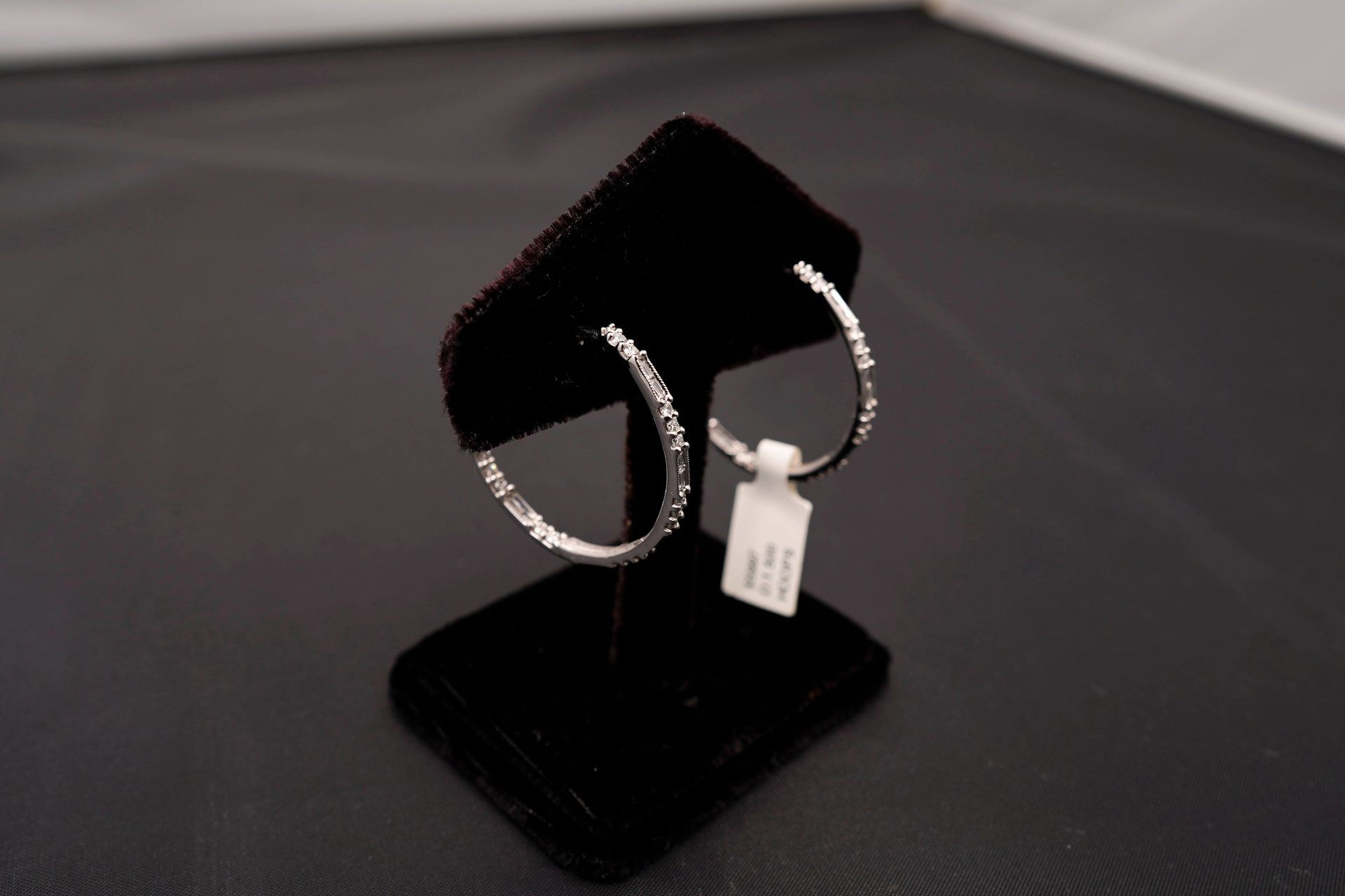 A pair of diamond hoop earrings displayed on a black stand with a small price tag attached.