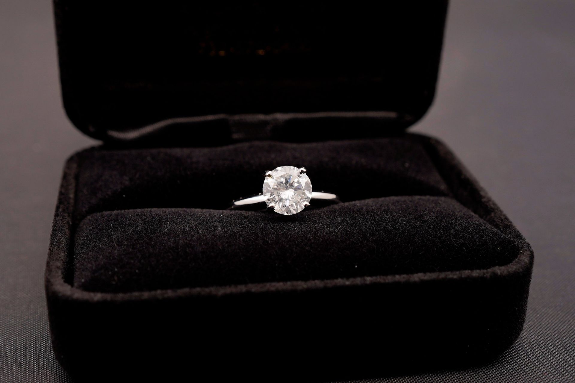 A solitaire diamond engagement ring centered in an open, black velvet jewelry box.