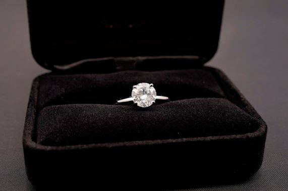 A solitaire diamond engagement ring centered in an open, black velvet jewelry box.