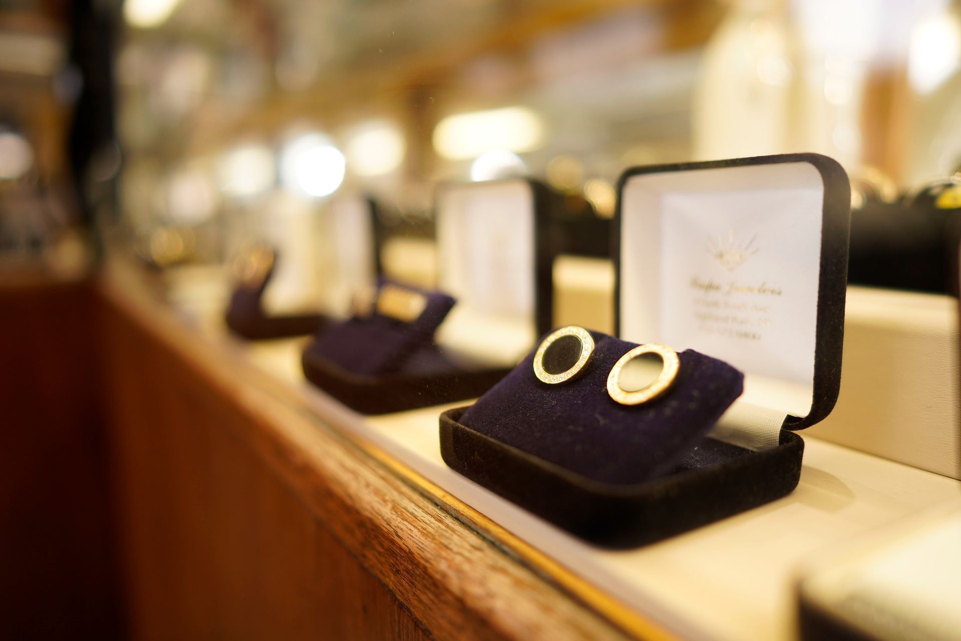 A row of jewelry boxes featuring round gold earrings displayed on a store counter.