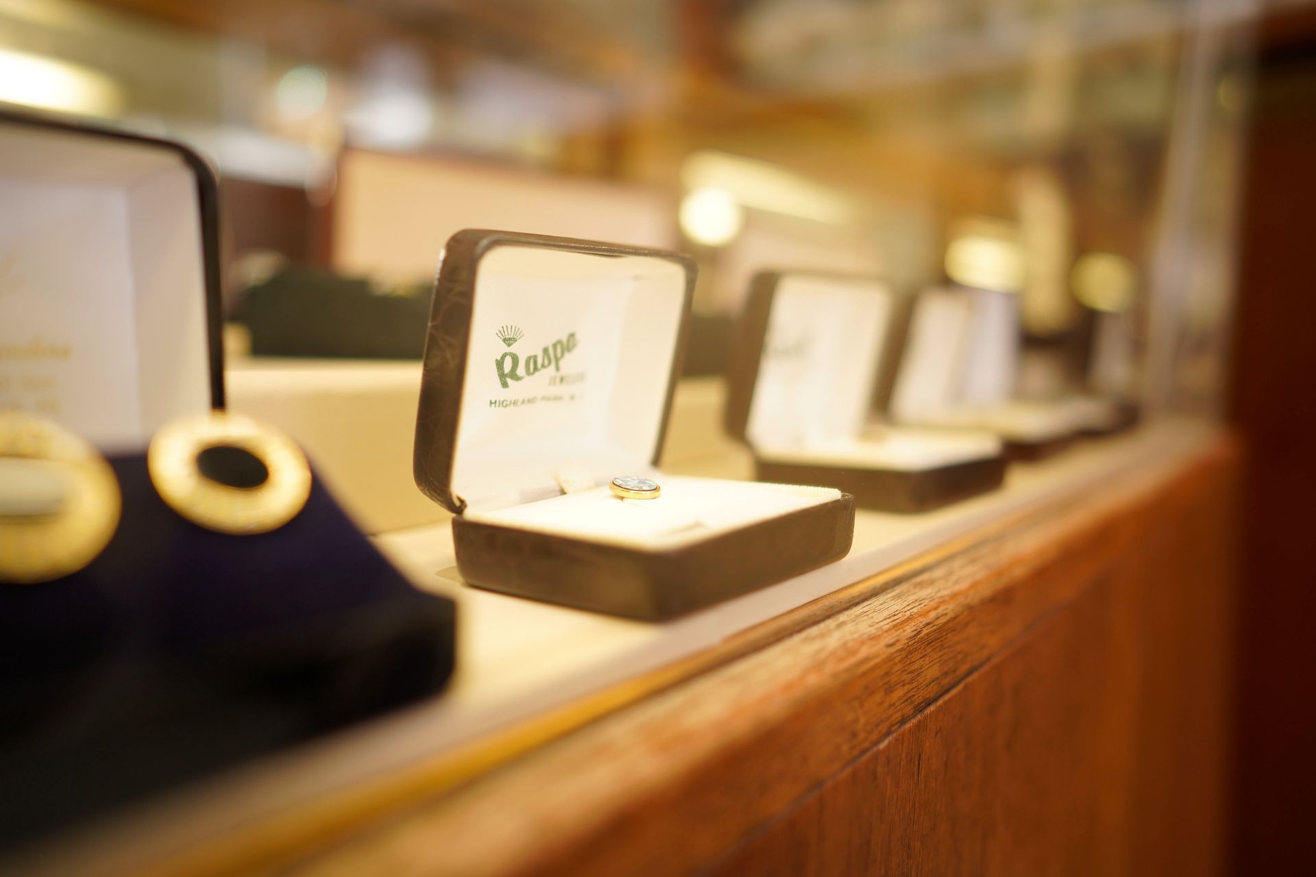 Open jewelry display boxes containing rings, lined up on a wooden counter inside a store.