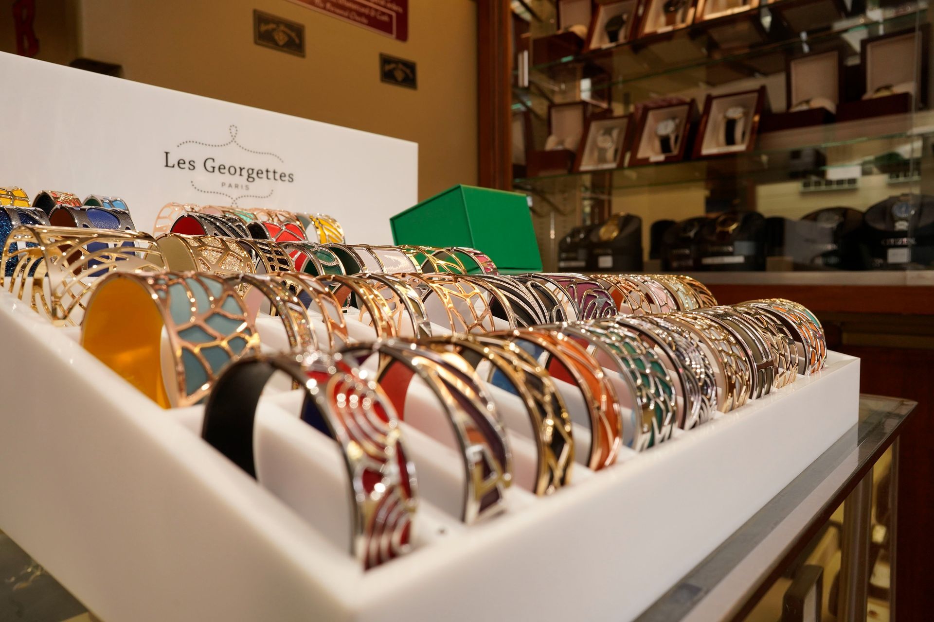 A white display tray holds rows of colorful, patterned Les Georgettes cuff bracelets inside a retail shop.