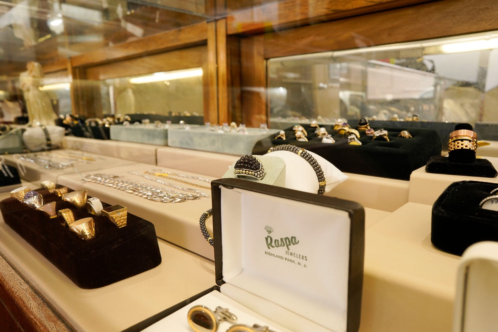 An array of rings and jewelry displayed inside a glass case on beige velvet trays.