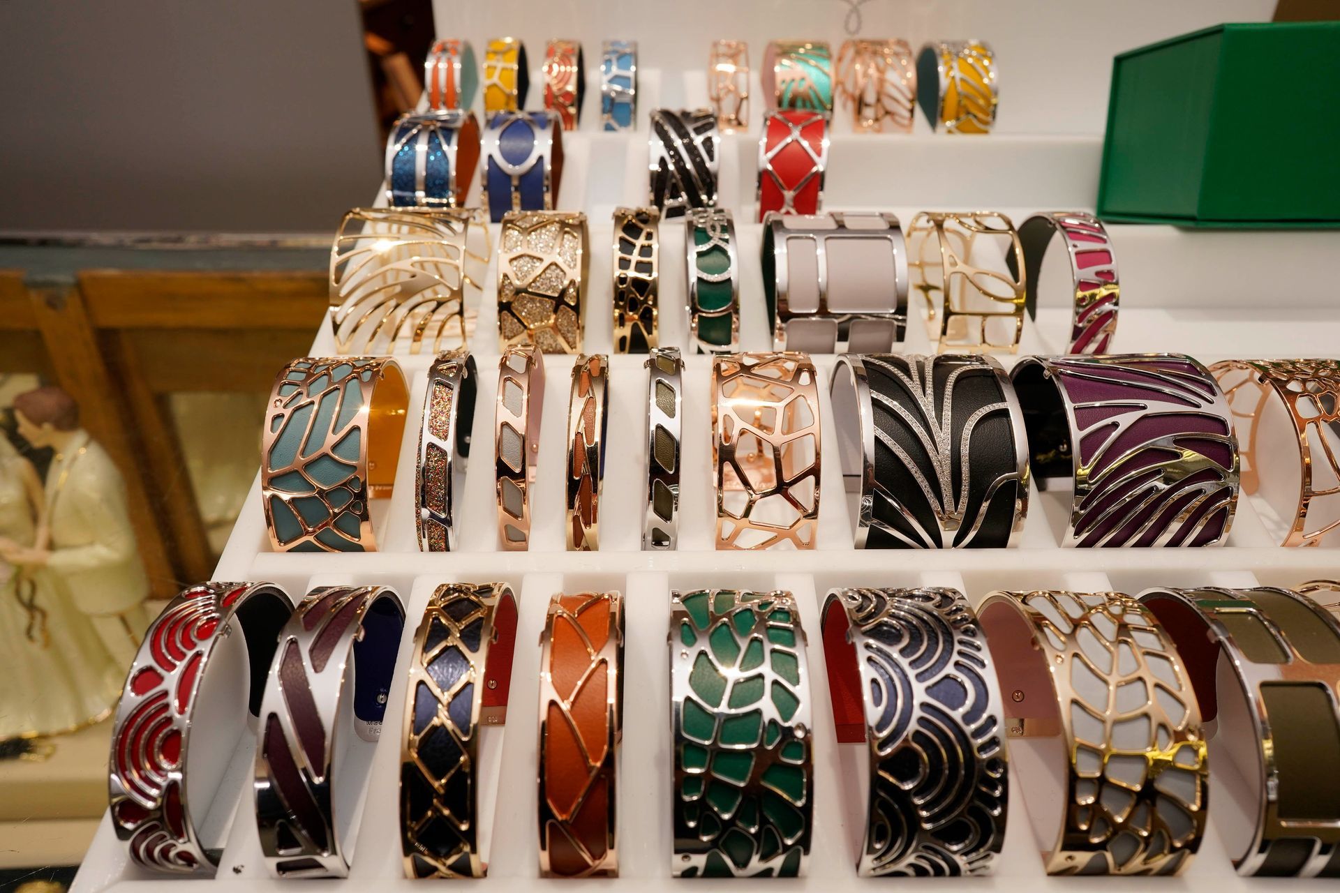 A retail display of numerous colorful, patterned metal cuff bracelets organized in rows on a white tiered stand.