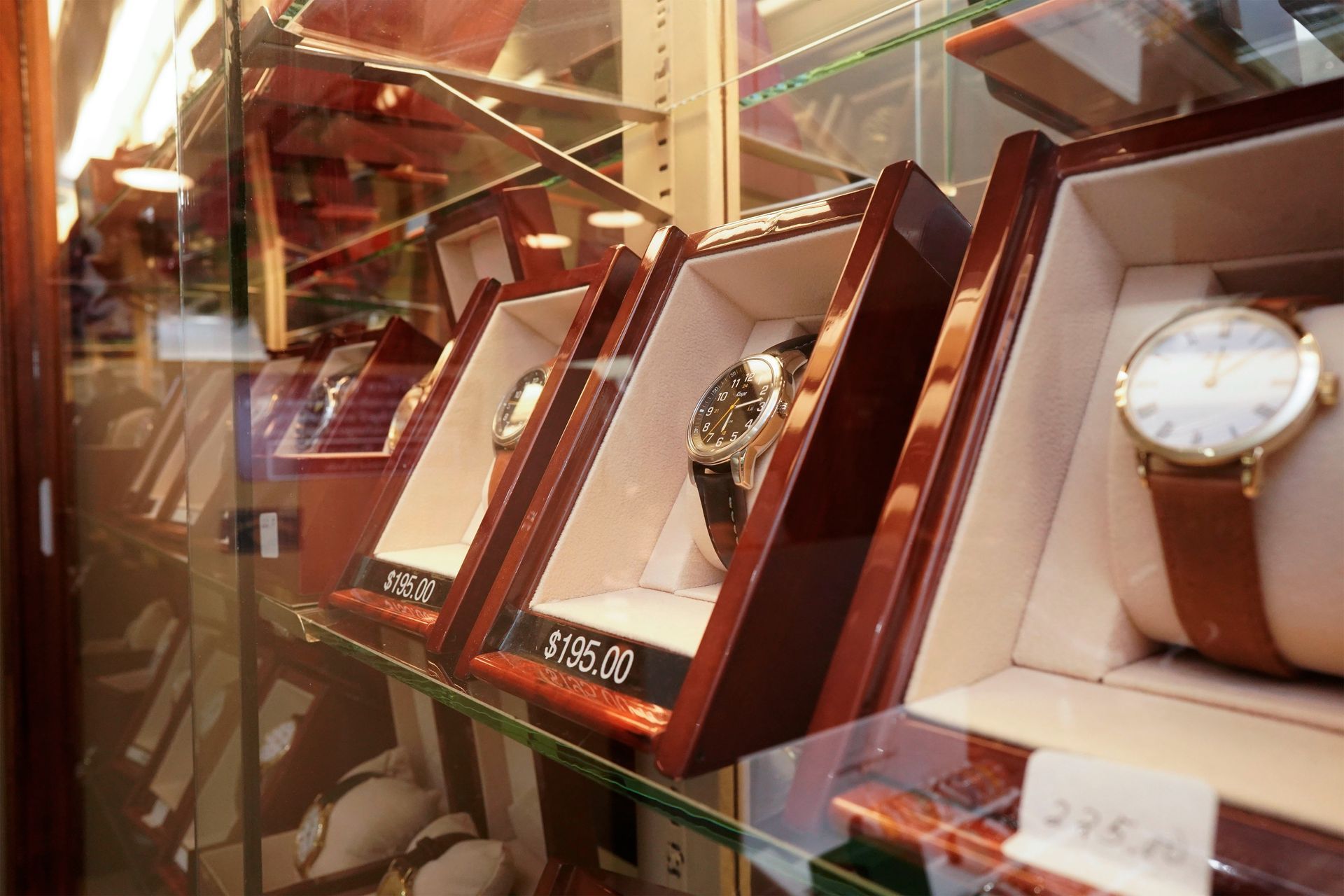 A display case featuring several luxury watches in wooden boxes with price tags on glass shelves.