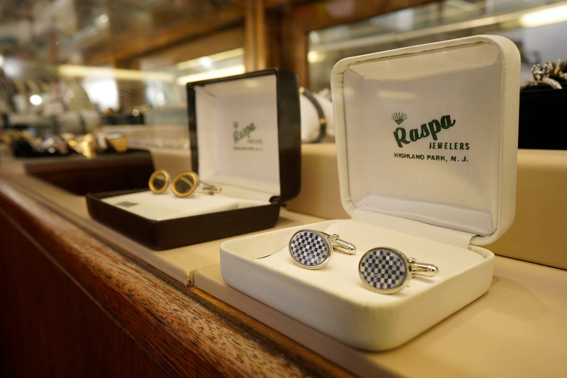 Two open jewelry boxes containing cufflinks on display on a wooden store counter.