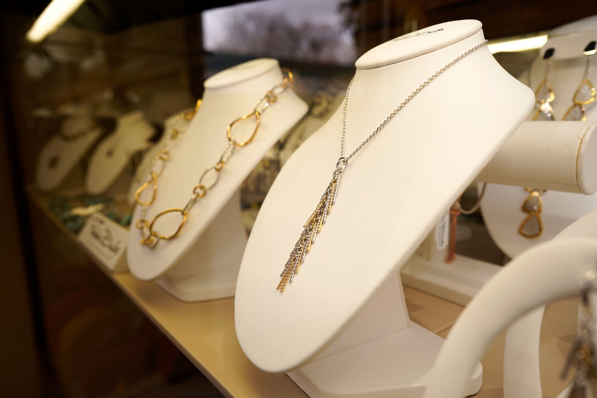 Several necklaces displayed on white stands inside a jewelry store showcase.