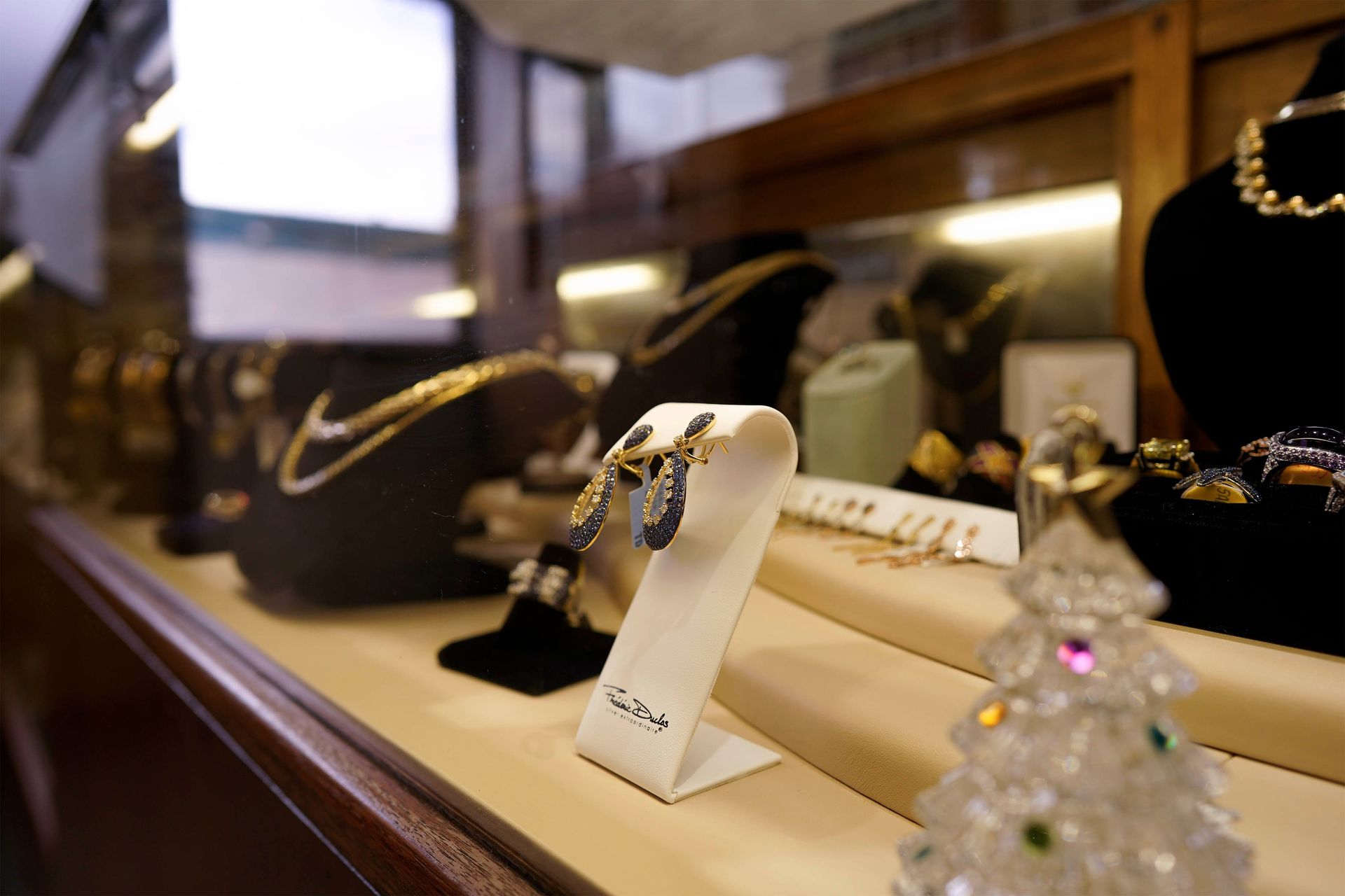 A jewelry store display case showing gold necklaces, earrings on a stand, and a decorative crystal Christmas tree.