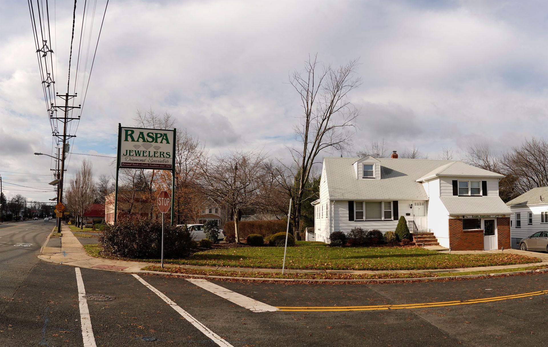 A white house with a brick base sits at a corner intersection next to a tall sign for Kasin's at a tree-lined street.