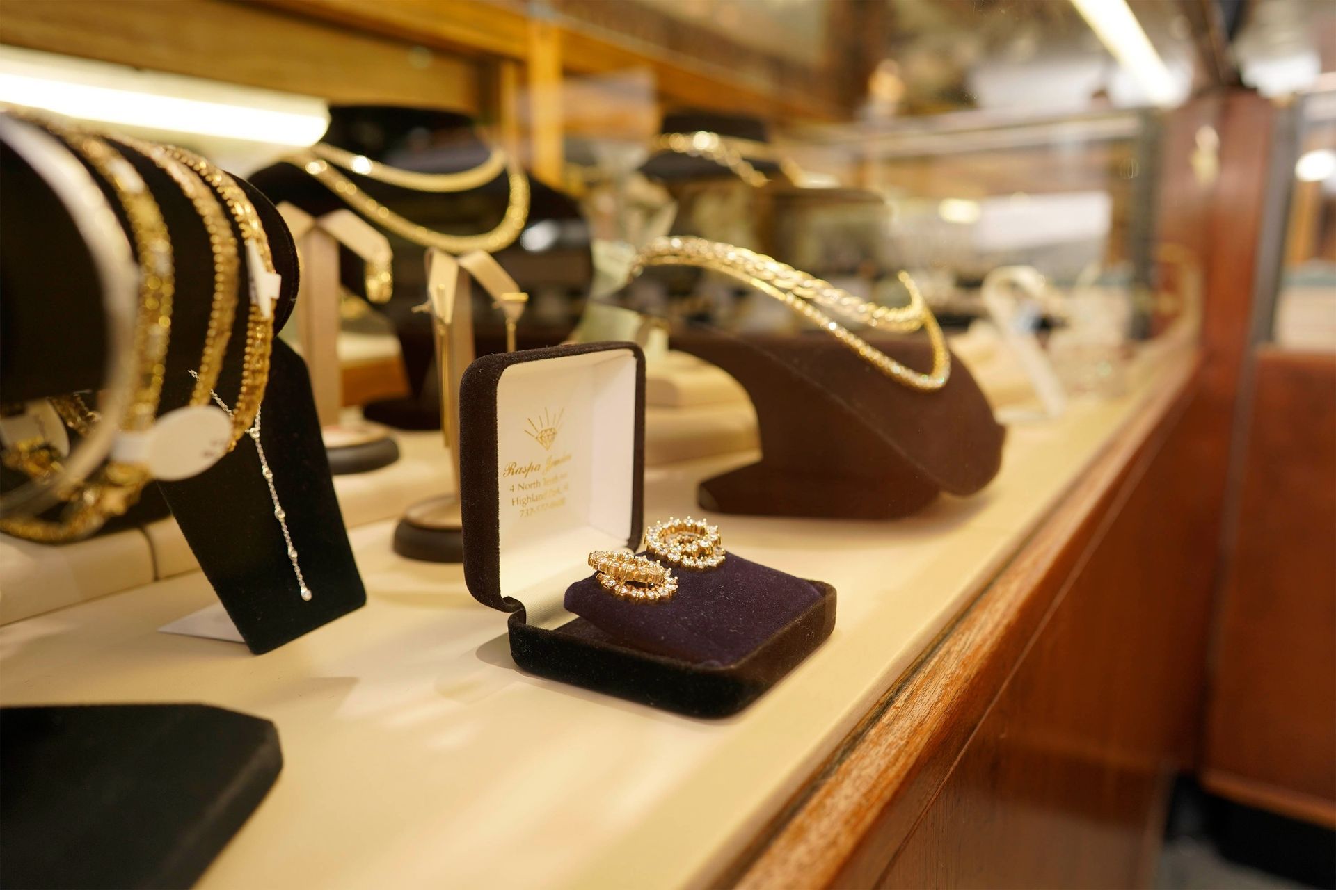 Gold jewelry, including earrings in a velvet box and necklaces on display stands, sits inside a glass display case.