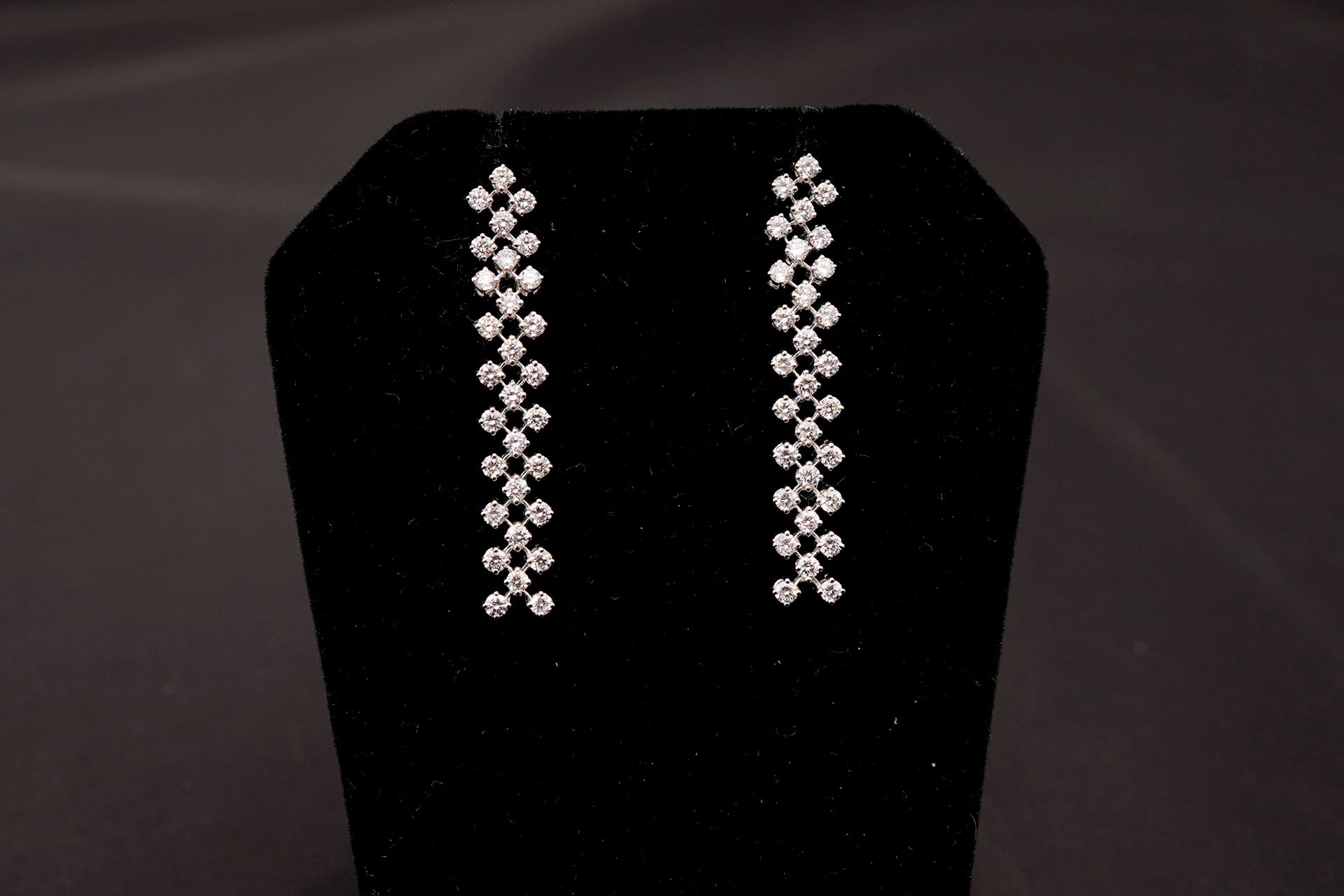A pair of long, dangling crystal earrings displayed on a black velvet jewelry stand.