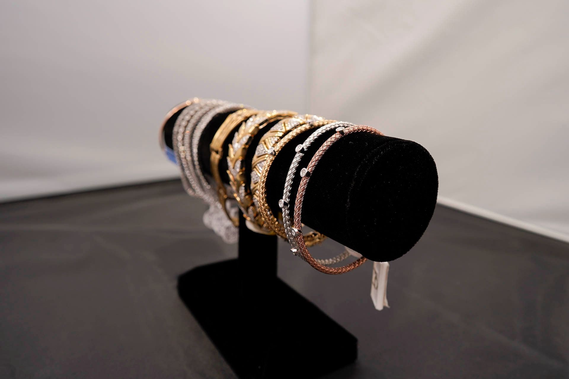 A black jewelry stand holding several metal bracelets in gold, rose gold, and silver tones against a white background.