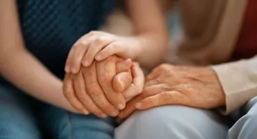 Two people holding hands in a supportive gesture on a couch