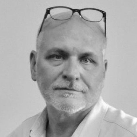 Black-and-white portrait of a bald man wearing glasses on his head, looking at the camera with a neutral expression