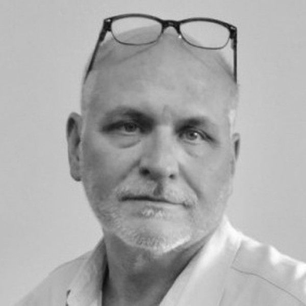 Black-and-white portrait of a bald man wearing glasses on his head, looking at the camera with a neutral expression