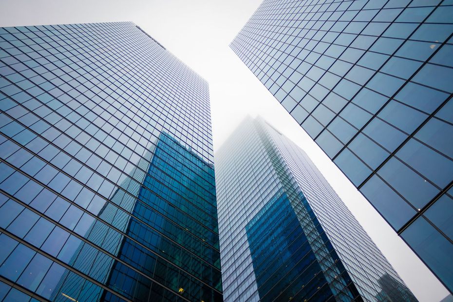 Looking up at reflective glass skyscrapers against a bright sky