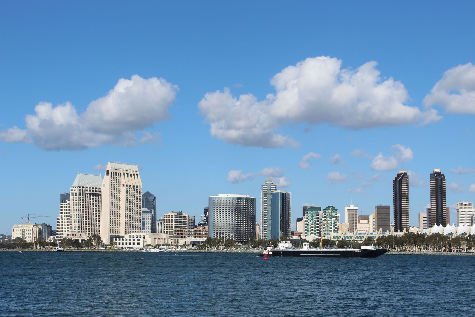City skyline across a body of water under a blue sky with scattered clouds