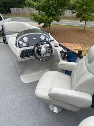 White pontoon boat captain’s chair and console with steering wheel and controls on a driveway.