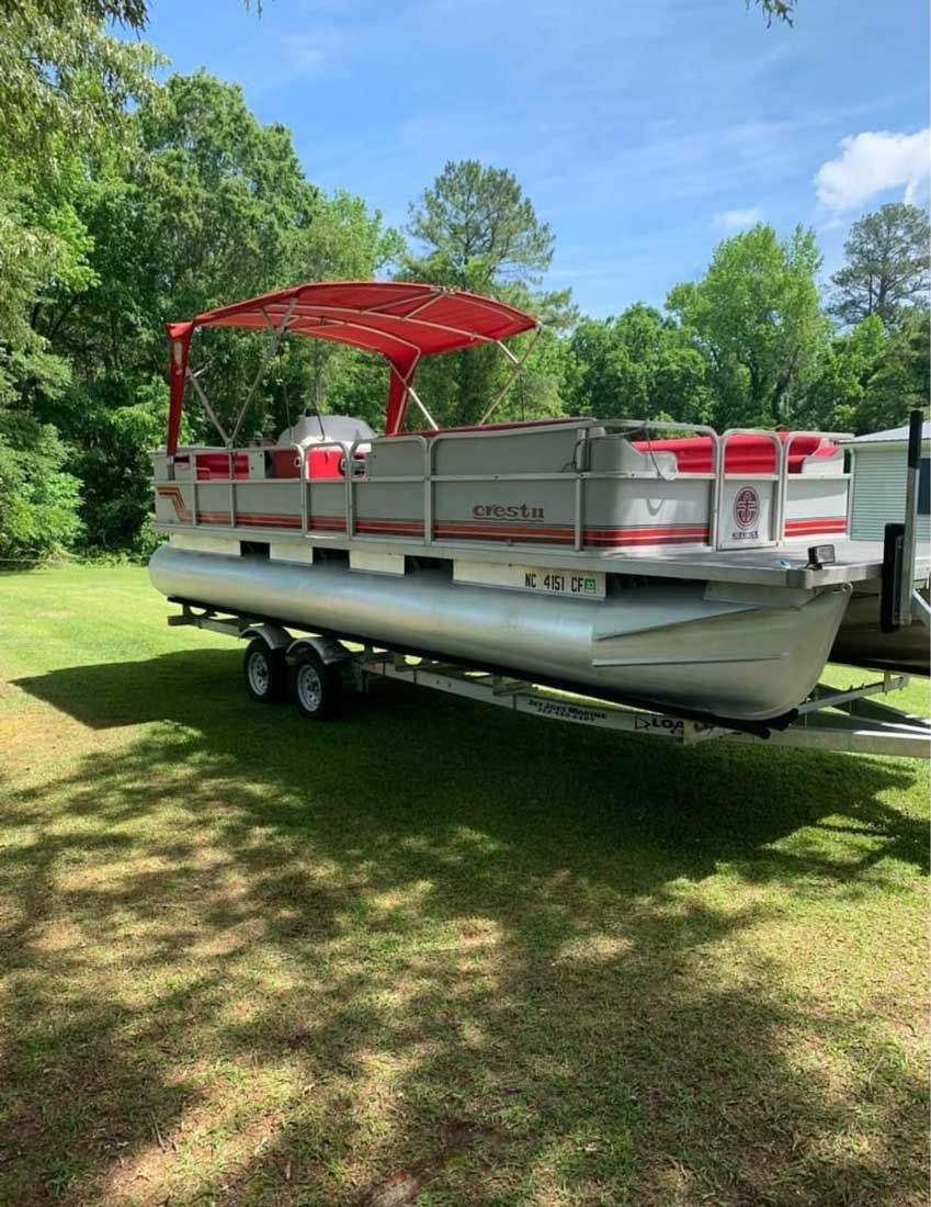 Pontoon boat with red canopy and bench seating parked on grass beside trees