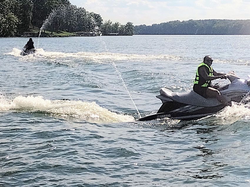 Person riding a jet ski on a lake, towing a wakeboarder behind across choppy water.