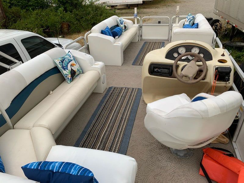 Pontoon boat interior with white seats, blue accents, tan carpet, and a helm console