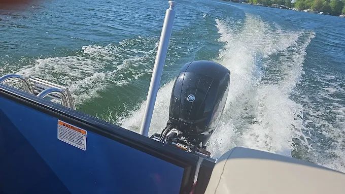 View from a boat’s stern: blue motor and foamy wake cutting across calm water.