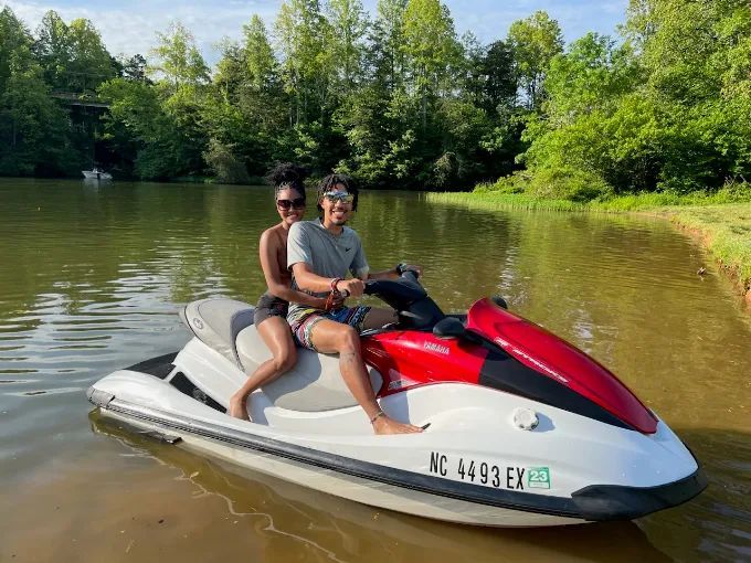 Two people riding a white and red jet ski on a calm lake near a wooded shore