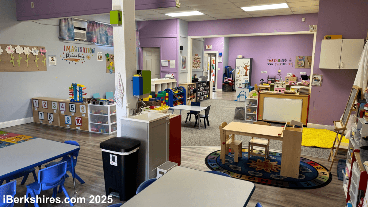 Interior of a brightly lit preschool classroom; lavender walls, small tables, toys, and storage cabinets.