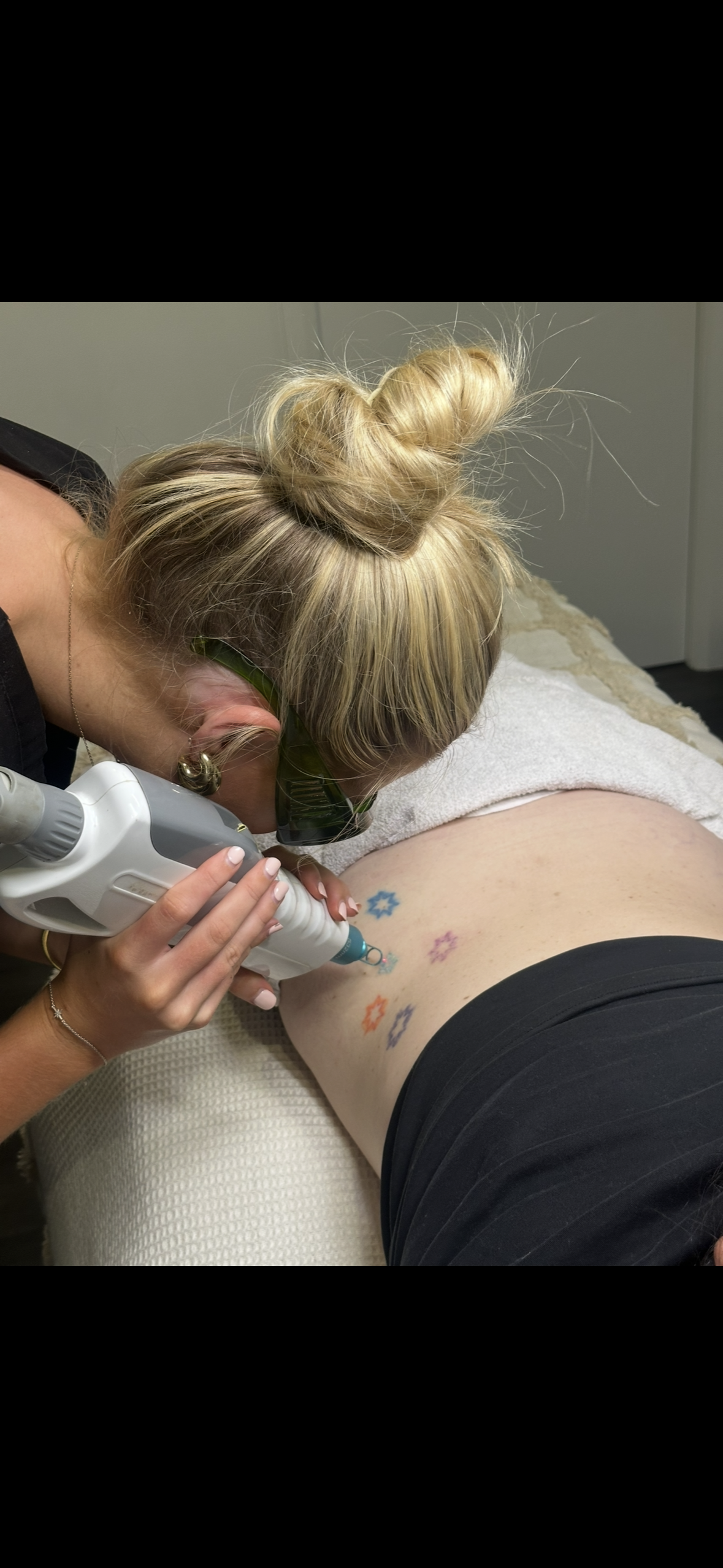Person tattooing a floral design on a client’s lower back with a handheld machine — Vanity Skin and Beauty Forster in Forster, NSW