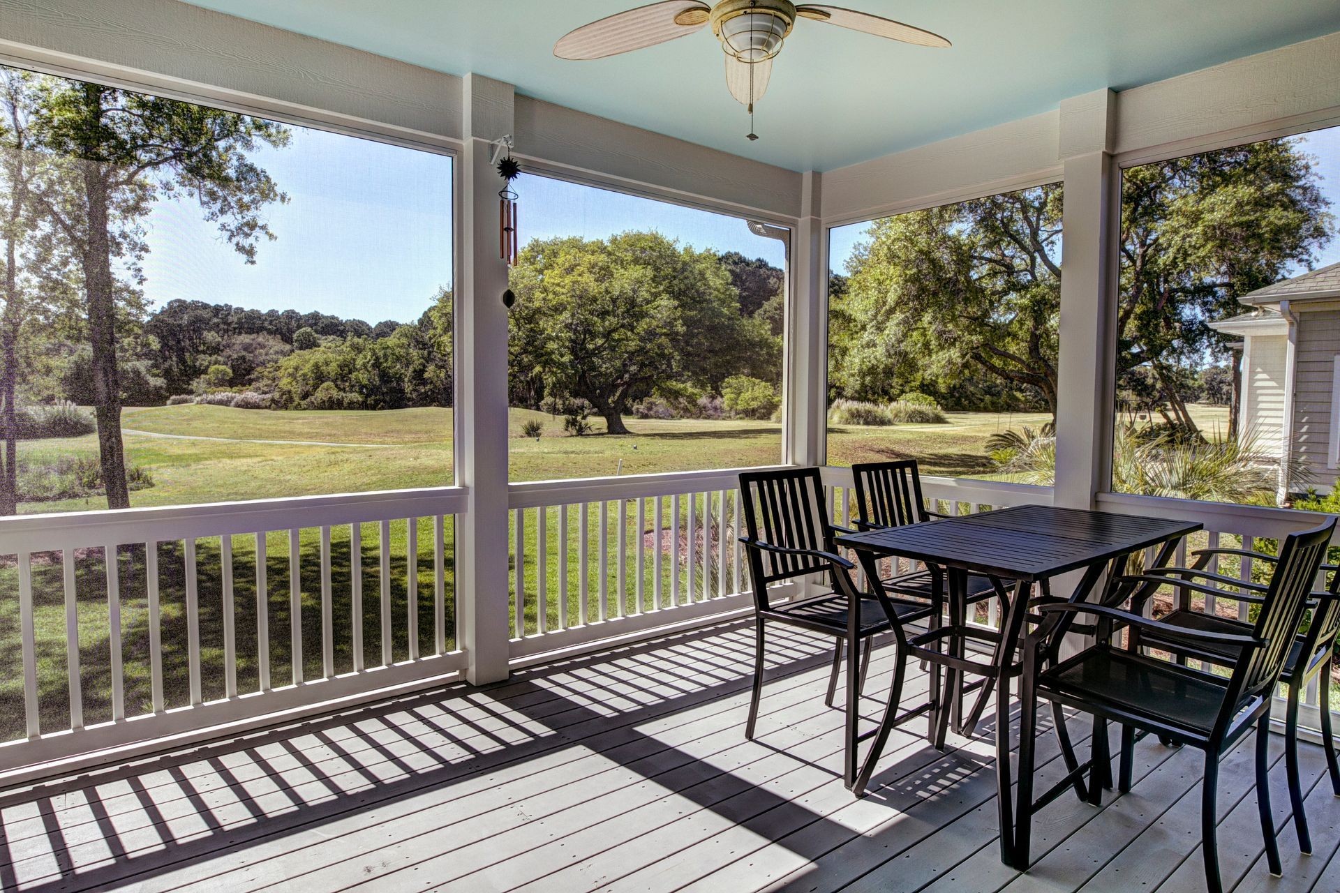 Covered porch with black patio table and chairs overlooking a sunny lawn and trees