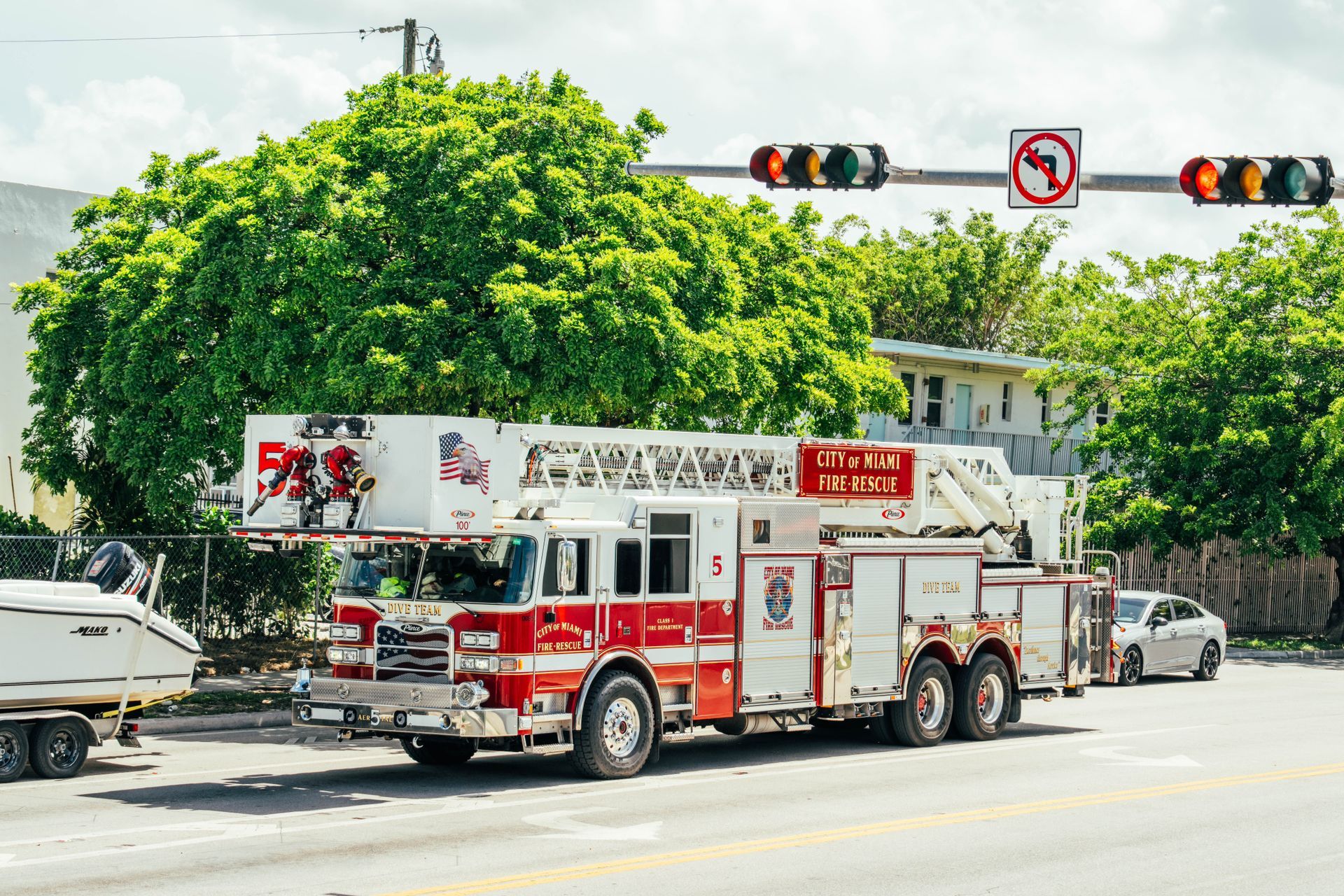 Fire truck at an intersection beside a large green tree, with traffic lights overhead.