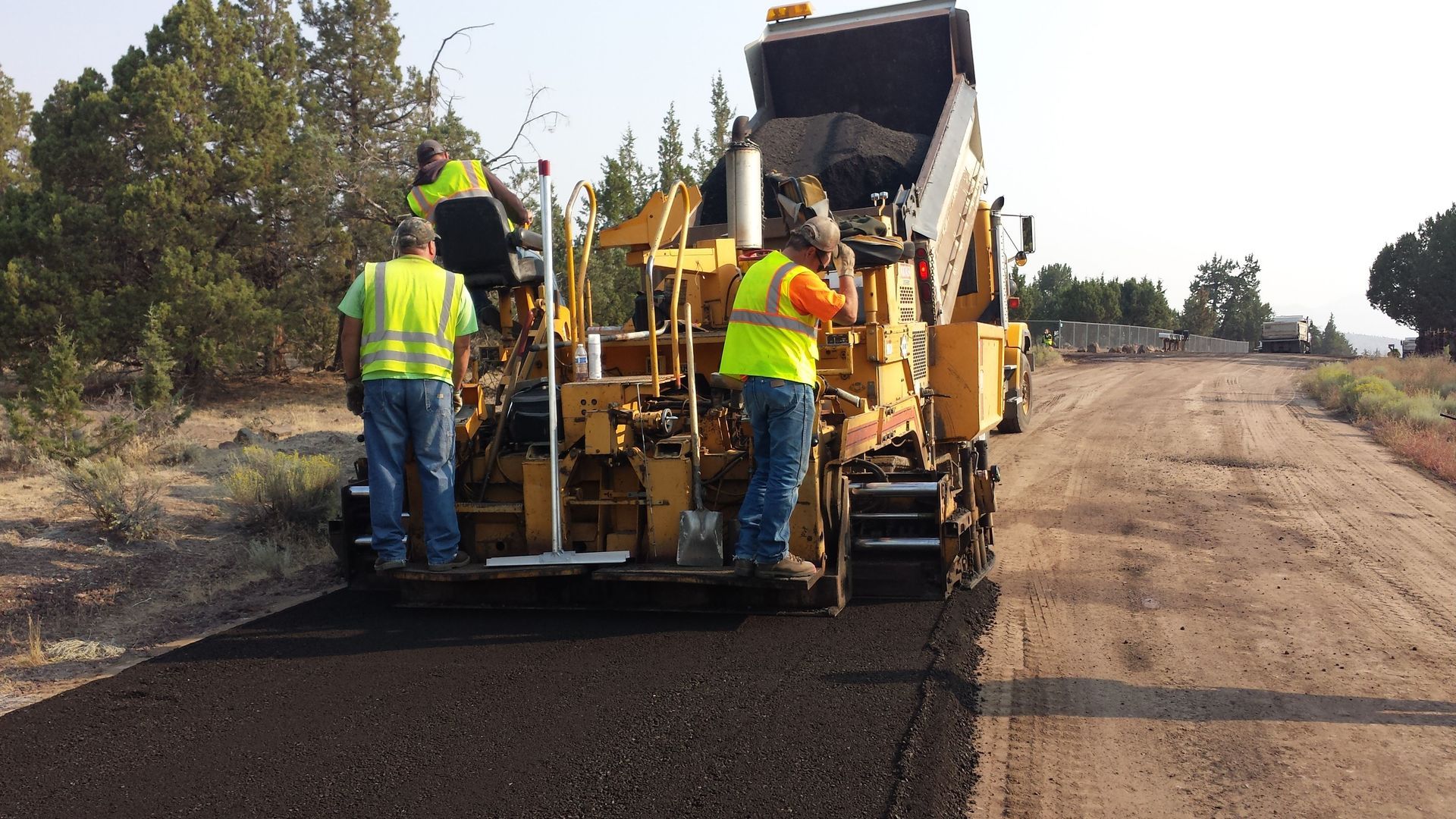Road crew paving a rural road with an asphalt machine and workers in safety vests