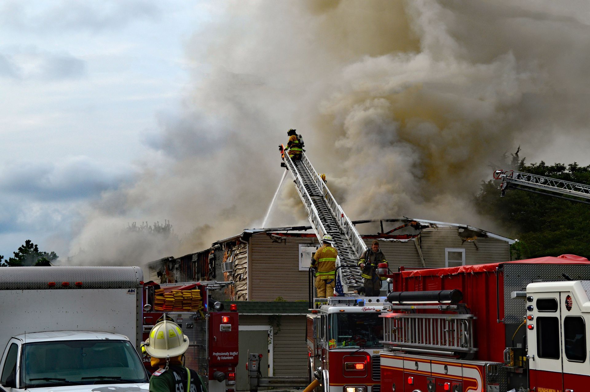 Firefighters battle a large warehouse blaze with ladders and trucks amid heavy smoke.