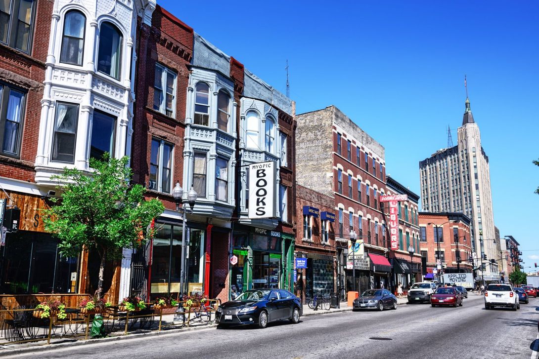 A row of buildings on a city street with cars driving down it.