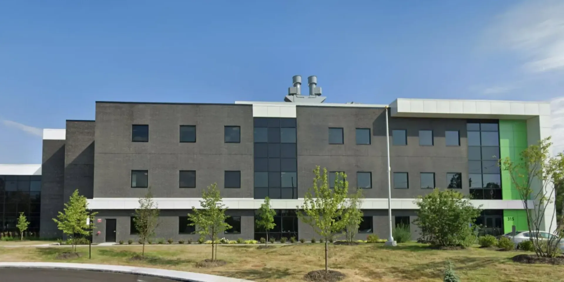 Immeuble commercial moderne à plusieurs étages, en briques grises, avec des finitions blanches et un mur d'accent vert vif, sous un ciel bleu clair.