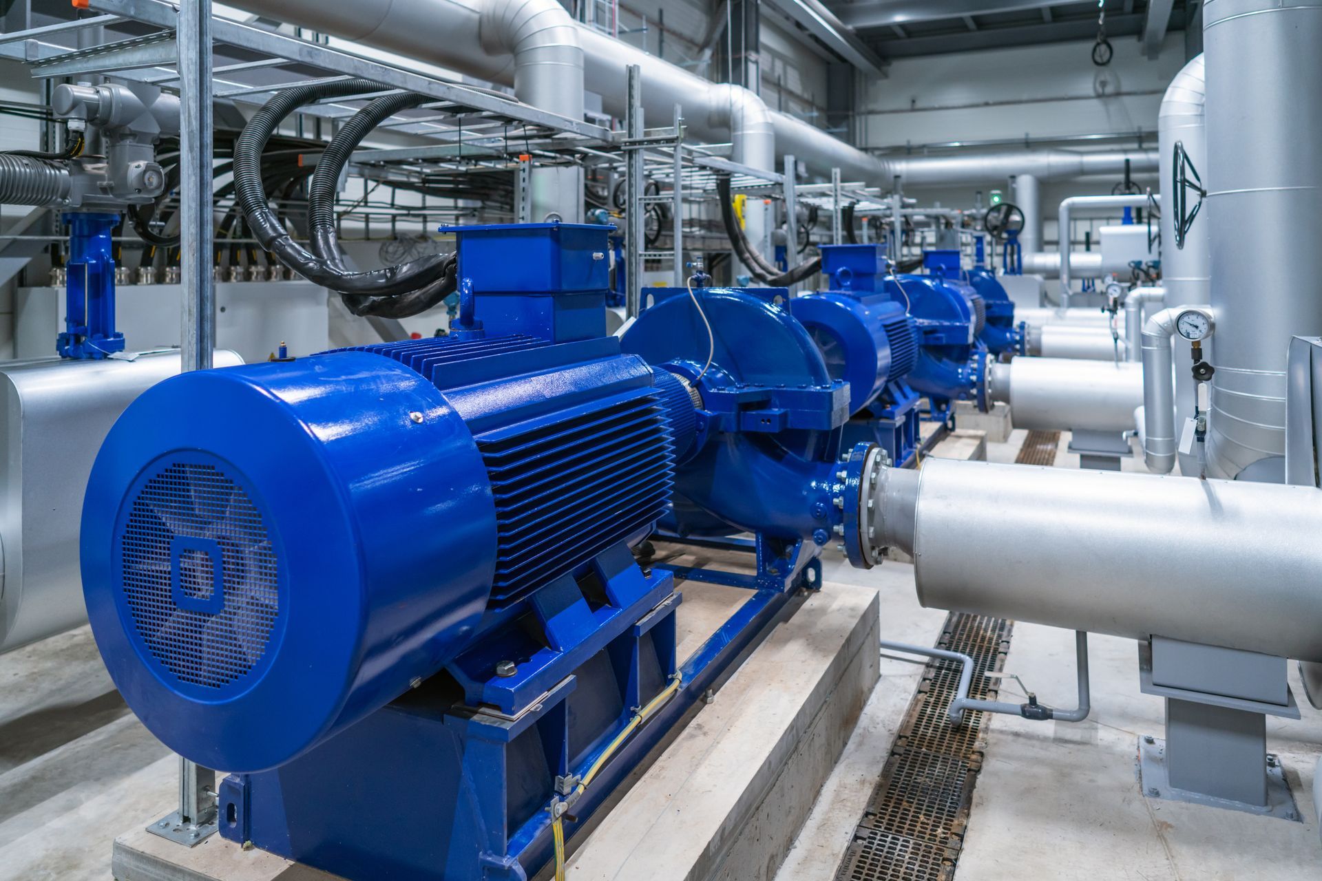 Des moteurs de pompes industrielles bleu vif sont reliés à des tuyauteries argentées dans une installation moderne et spacieuse.