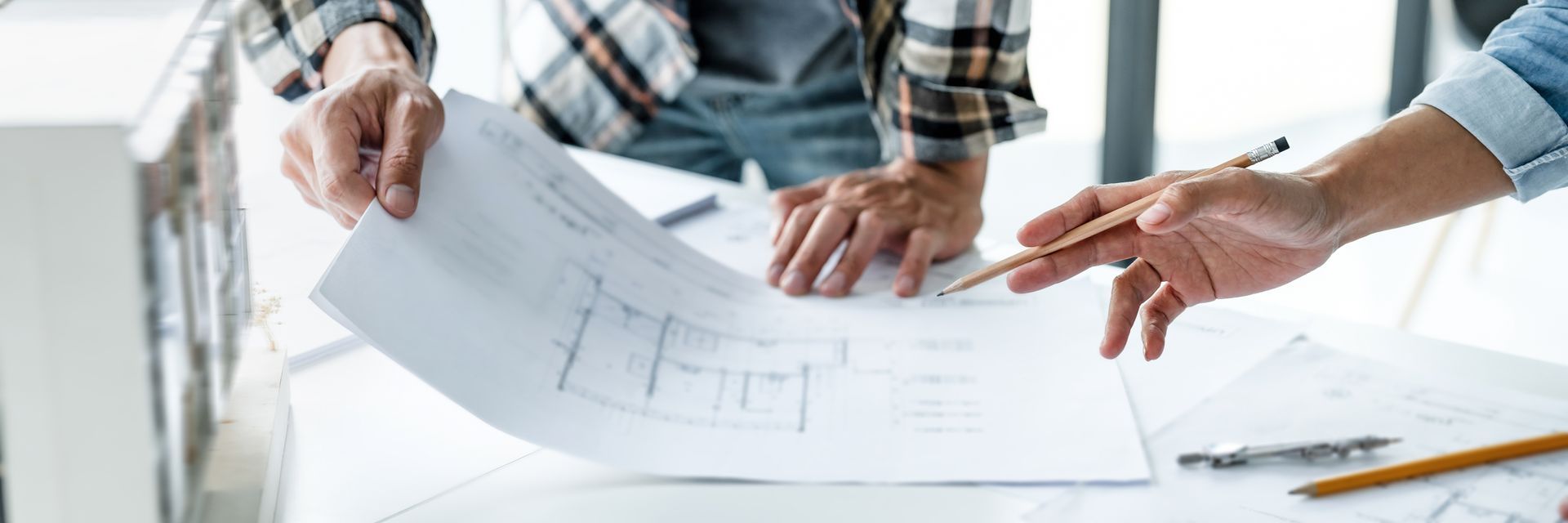 Deux personnes examinent des plans architecturaux sur un bureau, l'une d'elles pointant un détail précis au crayon.