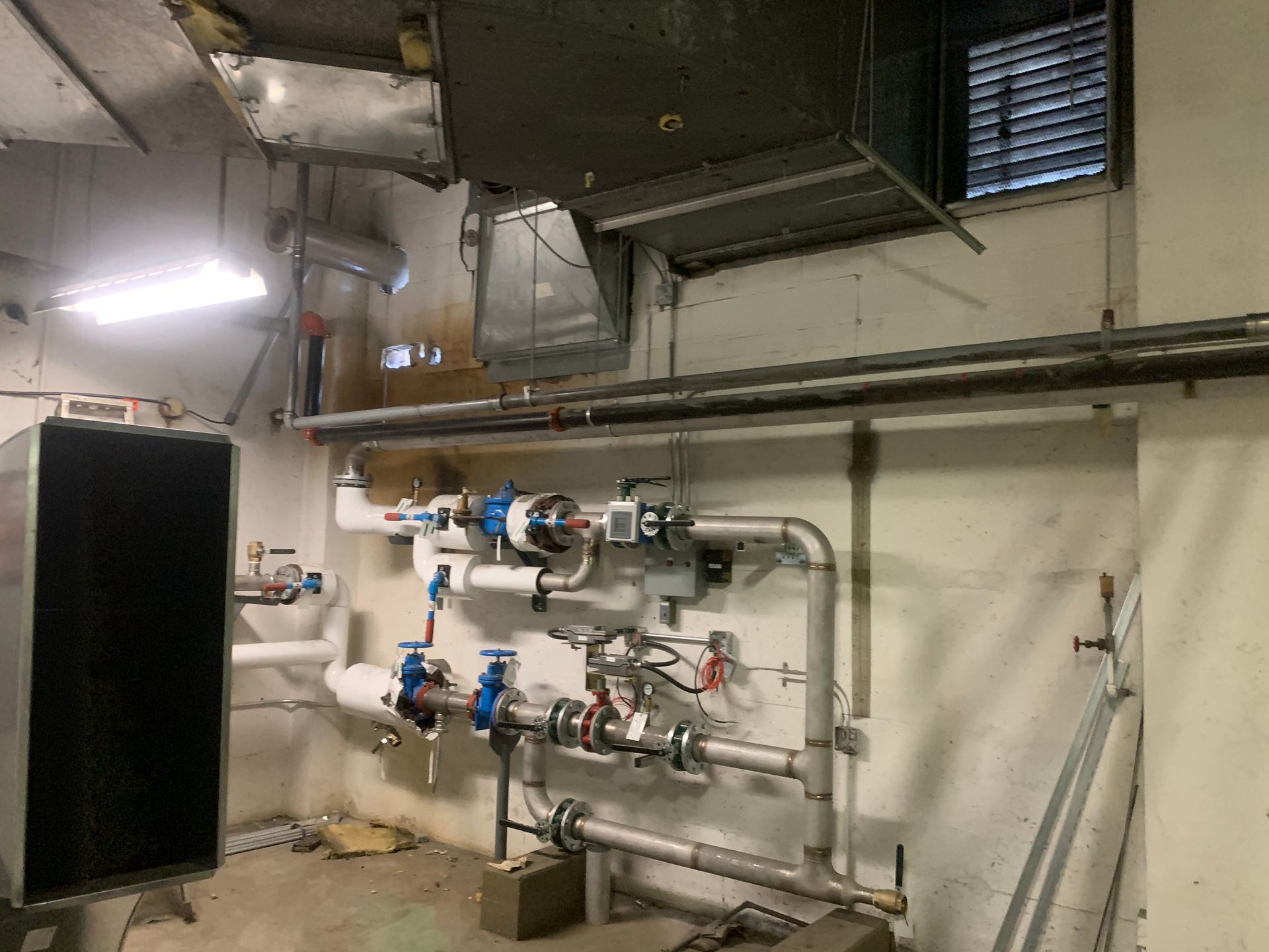 Sous-sol industriel avec tuyauterie, vannes et compteurs fixés sur un mur en béton