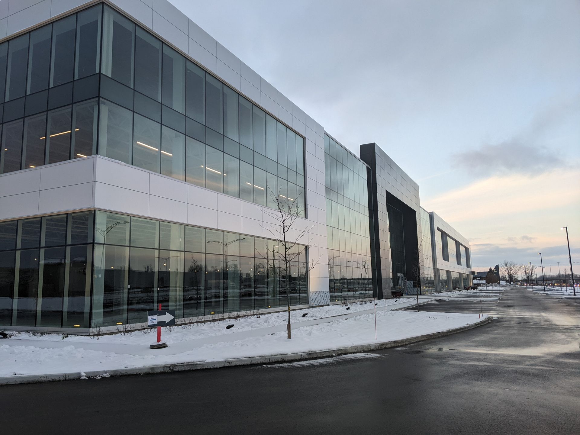 Un immeuble de bureaux moderne de trois étages avec une façade en verre, se détachant sur un ciel nuageux au-dessus d'un sol saupoudré de neige.