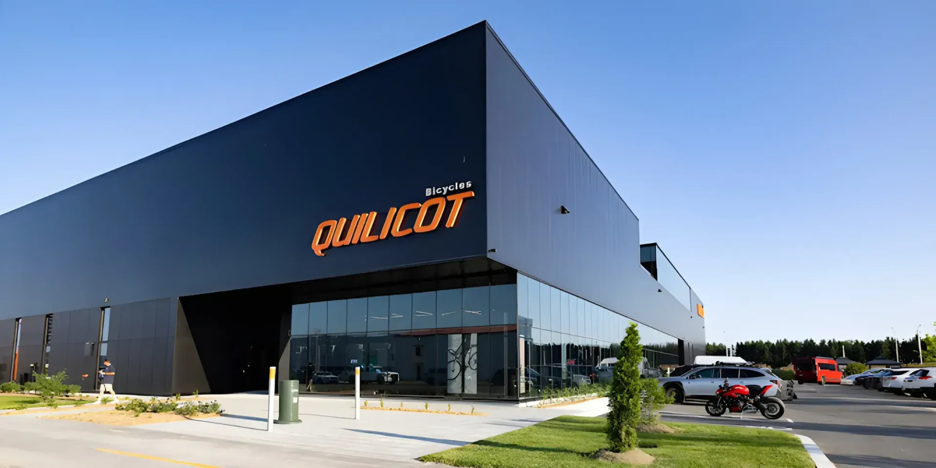 Un bâtiment commercial moderne, revêtu de noir, arborant le logo « QUALICOT », une entrée vitrée et un parking environnant.