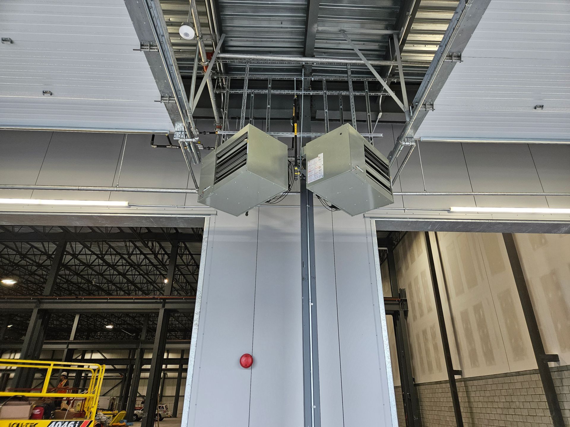 Deux appareils de chauffage industriels sont suspendus au plafond métallique d'un bâtiment commercial en construction.