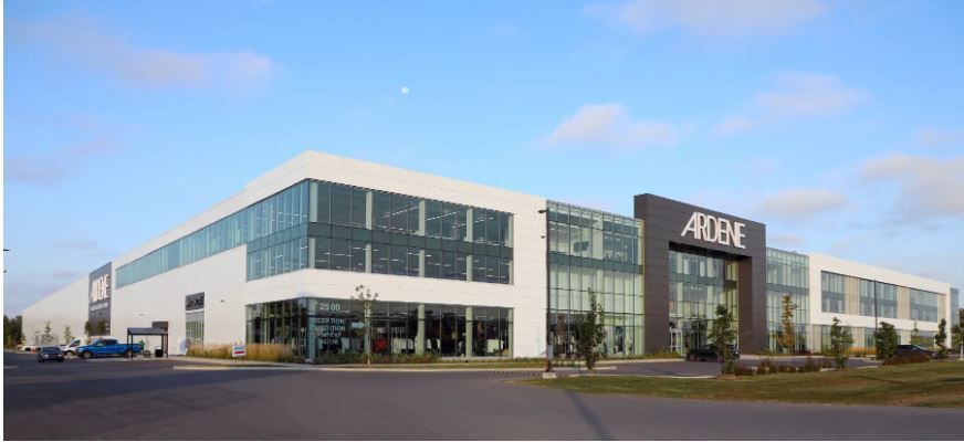 Un immeuble commercial moderne à plusieurs étages, aux murs blancs et aux fenêtres vitrées, arborant une enseigne Ardene, sous un ciel bleu.